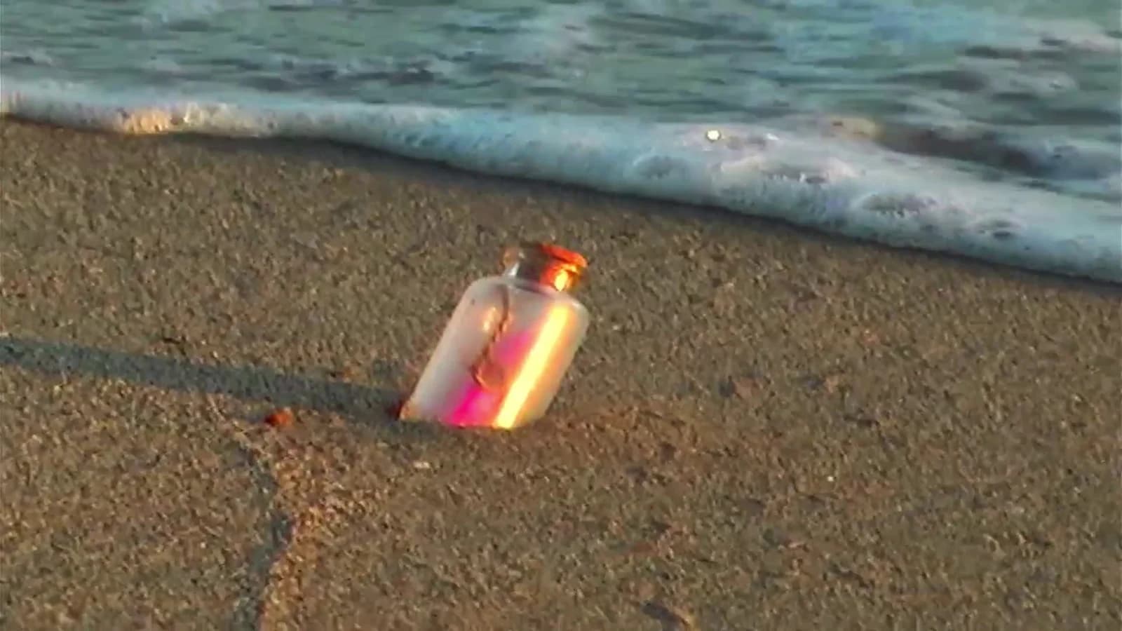 A pearlescent bottle in the sand by the sea
